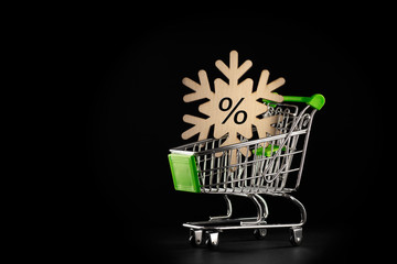 Big winter sale day or black friday. Blue snowflake in shopping cart, trolley on a dark background. Christmas sales, discount, gifts, delivery, shopping concept.