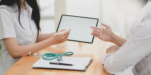 Cropped shot of young female doctor explain symptoms to her patient with tablet