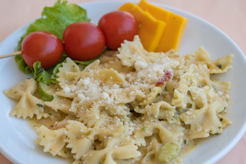 Pasta farfalle with cherry tomato and cheese in white plate, closeup