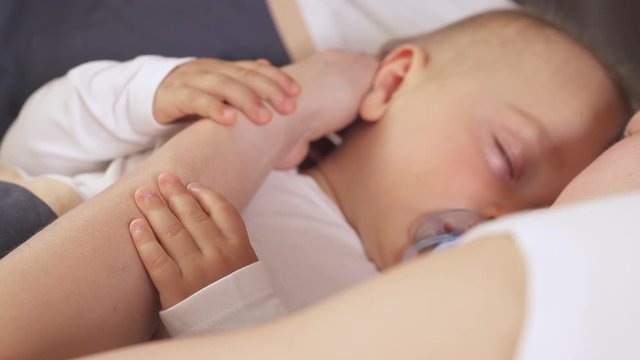 Close-up of a cute toddler boy peacefully sleeping in bed with his mother and ditching the soother. Nursing kid and parenthood concept