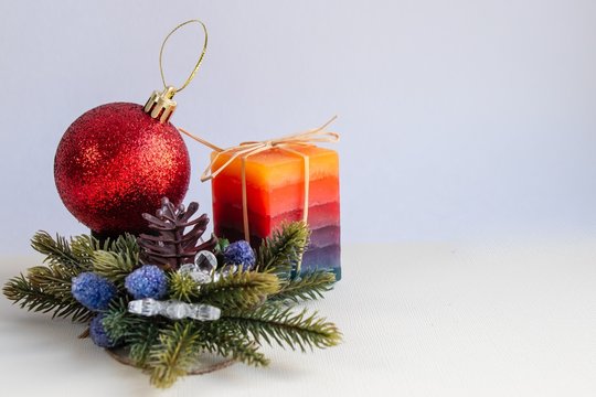 Decorative candle, red Christmas toy and fir branches on a light background. There is free space for writing text.