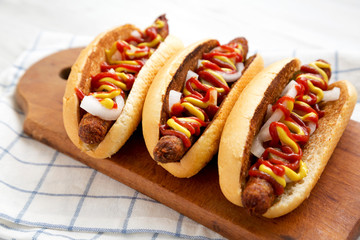 Homemade hot-dogs with chicken sausage, ketchup and mustard on a rustic wooden board, low angle view. Close-up.