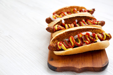 Homemade hot-dogs with chicken sausage, ketchup and mustard on a rustic wooden board on a white...