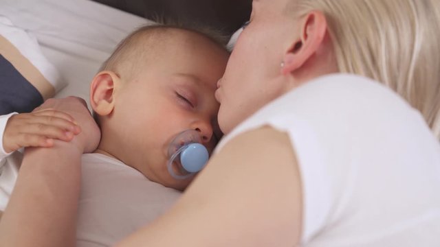 Close-up of caring mother gently kissing her peacefully sleeping son. Child is ditching the soother. Happy family concept