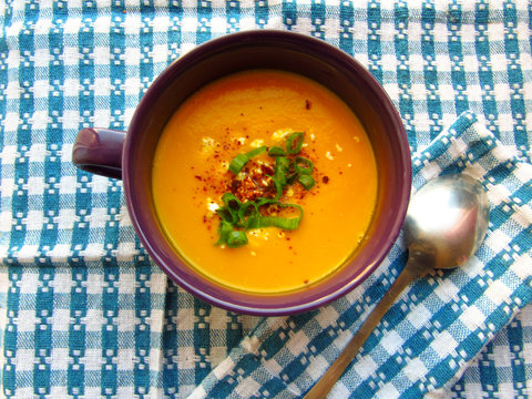 autumn cream of carrot and pumpkin served in purple crockery bowl on white and blue plaid mat