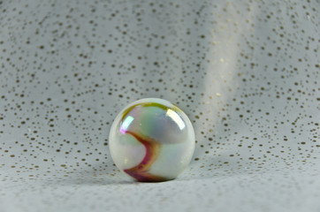 A large polished and shimmering marble, bullet of glass, in colour of nacre lying on a ground of white and gold sparkling texture