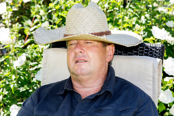 Man with straw hat has fallen asleep in the garden chair