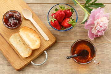 Cup of tea, homemade strawberry jam in bowl, fresh berries with toast on wooden background.