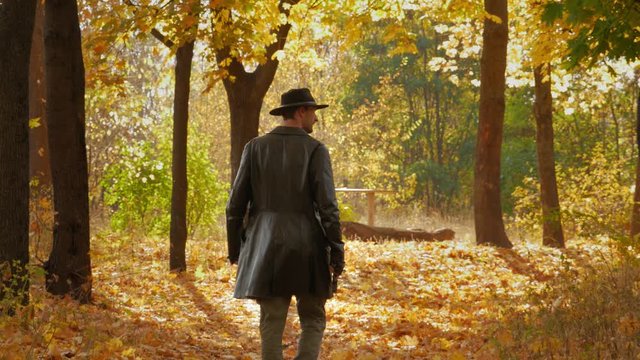 Dangerous cowboy with a gun in a leather coat walks through the autumn forest in search of his opponent