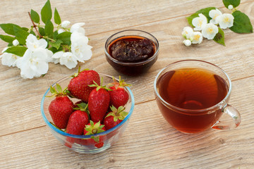 Glass cup of tea, strawberries with white jasmine flowers