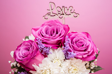 Word Love, love concept with pink rose flowers on a pink background with white flowers