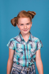 Emotional portrait of a little funny naughty girl with red hair  against  blue background