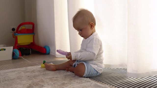Close-up of a curious baby boy playing with toy on the floor at home and crawling towards camera