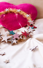 Star christmas wreath in soft colors over white and soft blanket and pink heart cushion. Soft Christmas decoration.