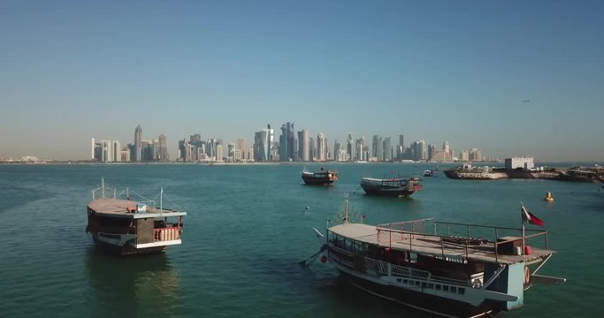 Aerial flying forward view of Doha boat harbour with skyscrapers and West Bay business district in the background, futuristic capital city of Qatar, corniche on the waterfront