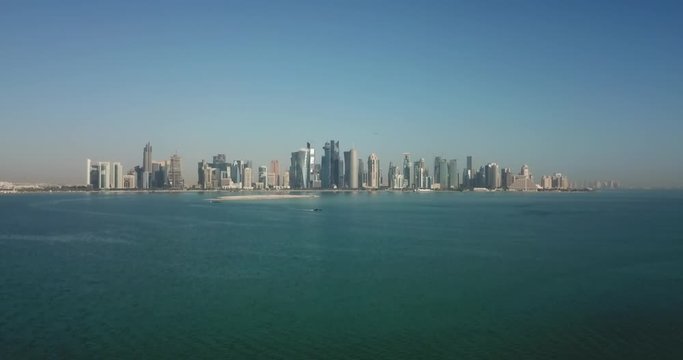 Aerial rising day view of Doha corniche and business district in Qatar, with skyscrapers and urban skyline in the background on the waterfront of the persian gulf, west bay area