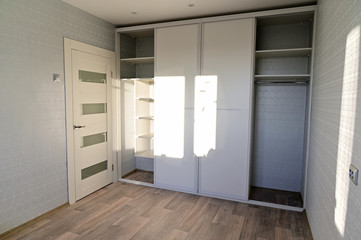 Photo of a white built-in wardrobe with sliding doors in a room with clear sun from the window.
