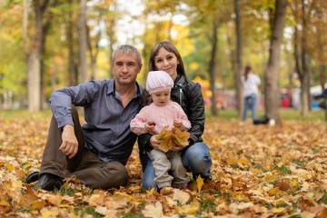 Naklejka na ściany i meble Happy family together in autumn garden/park. Parents with their children are sitting on coverlet in park. Outdoor in full height photo. Family concept