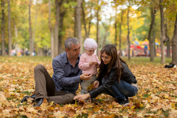 Happy family together in autumn garden/park. Parents with their children are sitting on coverlet in park. Outdoor in full height photo. Family concept