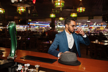 Handsome well-dressed arabian man with glass of whiskey and cigar posed at pub.