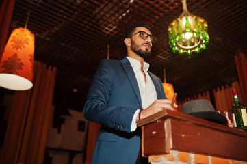 Handsome well-dressed arabian man with glass of whiskey and cigar posed at pub.