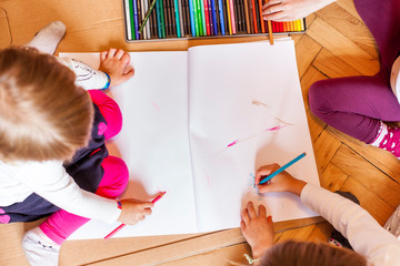 Kinderaktivität. Kinder sitzen am Boden und malen mit Buntstiften. Kids indoors activity. top-view.