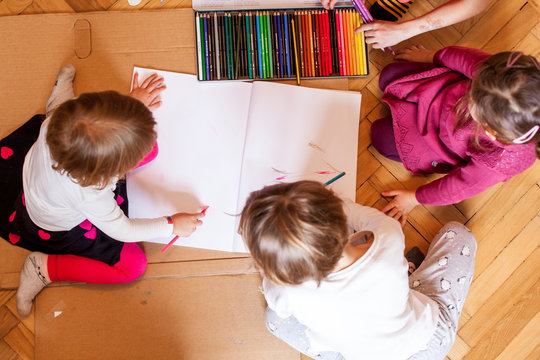 Kinderaktivit&auml;t. Kinder sitzen am Boden und malen mit Buntstiften. Kids indoors activity. top-view.