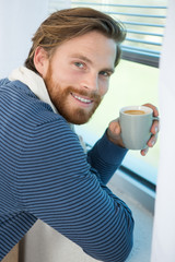 portrait of young man sitting near window with coffee