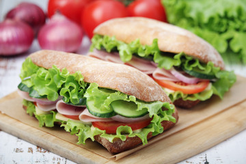 Two sandwiches with fresh vegetables, ham and cheese in ciabatta bread