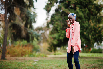 Fototapeta premium Young modern fashionable, attractive, tall and slim african muslim woman in hijab or turban head scarf and pink coat posed at park.