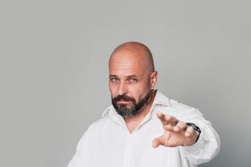 Handsome serious middle-aged man in a white shirt shows a finger at the camera on a gray background with copy space