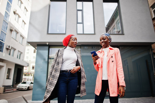 Two young modern fashionable, attractive, tall and slim african muslim womans in hijab or turban head scarf and coat posed with mobile phones.