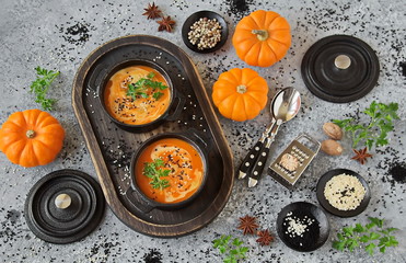 Pumpkin soup with cream in a cast iron pot. Homemade pumpkin soup served with cream, butter, sesame and parsley on a grey concrete background