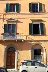 Fototapeta na wymiar Orangish wall with windows and balcony and green shutters of an antique building in Pisa, Italy.