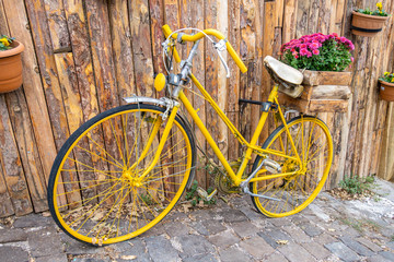 Fototapeta na wymiar Yellow bike with a basket of flowers near old rustic wooden wall. Vintage bicycle with wooden box of purple flowers.