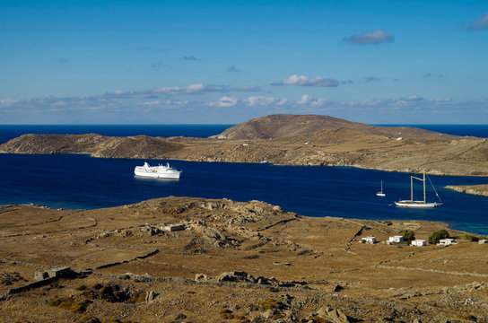 Panorama von zerklüfteter Felsenküste mit Ruinen und Kreuzfahrtschiff Ocean Majesty und Segelyacht Chronos auf blauem Meer auf griechischen Inseln in Ägäis während Kreuzfahrt