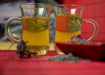 Herbal cold tea with lavender and oregano in glass cups on a yellow and red background.