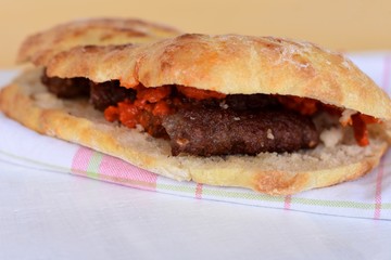 Slavic Bosnian Croatian Serbian burger, Traditional fast food from Balkan cuisine - juicy cevapi made of minced meat and served with red sauce Ajvar in a special bun, lepinja or somun