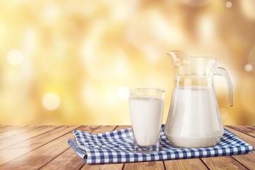 A glass of milk and a milk jug on plaid tablecloth