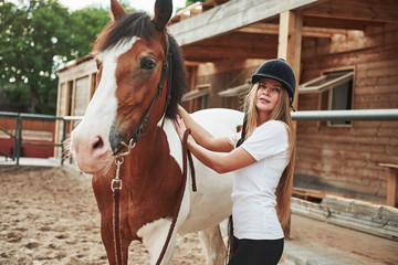 In black protective helmet. Happy woman with her horse on the ranch at daytime