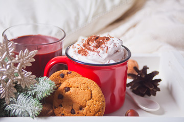 Red mug of cocoa on the white tray on the bed early winter morning