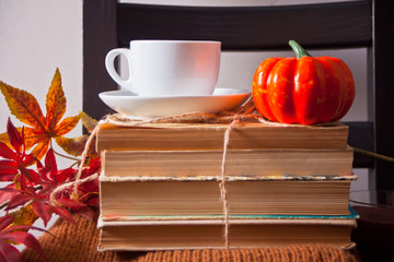 Cup of coffee, autumn leaves, small pumpkin, old books on the wooden black chair. Autumn harvest. Autumn concept