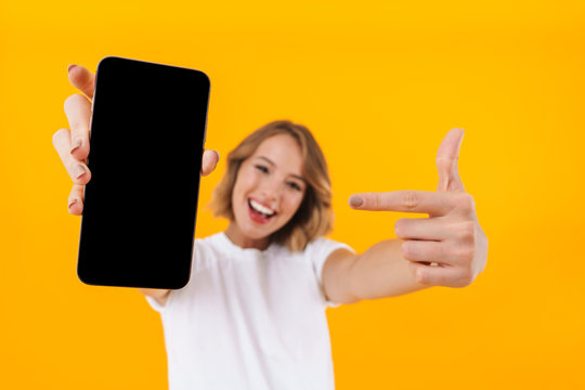 Image of young blond woman pointing finger at smartphone in hand