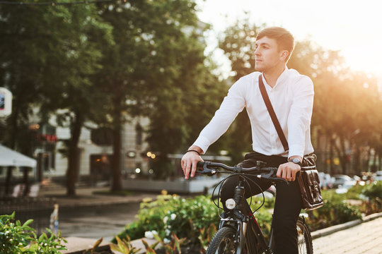 Summer green trees at background. Businessman in formal clothes with black bicycle is in the city