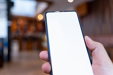 Man holding smartphone with white blank screen at coffee shop .Blank screen mobile phone for graphic display montage.empty copy space for advertising.