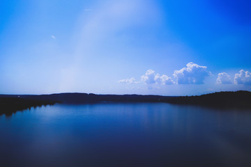 magical beauty river with a blue smooth surface. There is a clear sky above the water with one white cloud, and in the distance the earth and forests are visible. no unnecessary details, minimalistic 