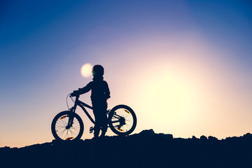 Silhouette of a little girl with a bicycle at sunset