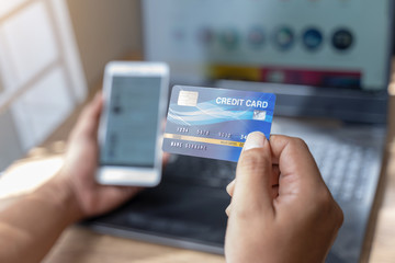 Man holding mock up banking card while using smartphone and laptop computer.Online shopping, online payment,buy and sell products & services.