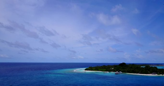 Aerial view from over tropical water looking out towards a small resort island in the Maldives