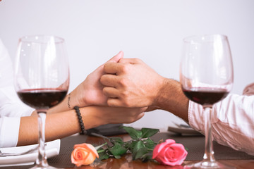 Male and female hands with roses. Closeup of couple hands, two glasses of red wine. Romantic couple holding each other's hand at dinner in a restaurant. Love, Marriage proposal and engagement concept.